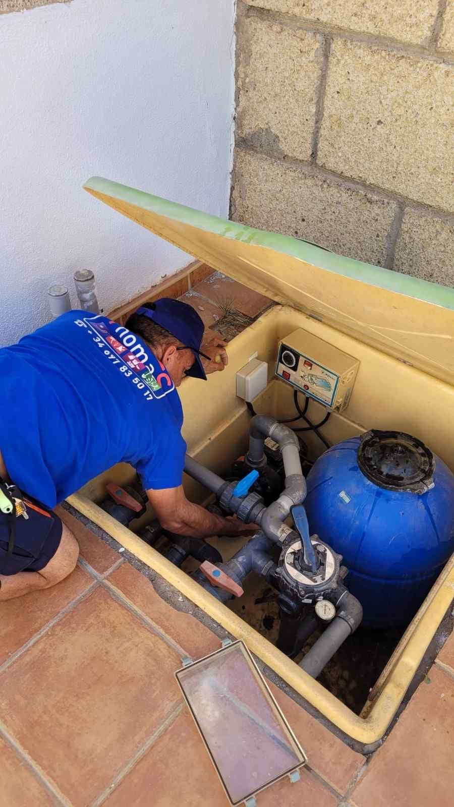 Un trabajador inspecciona el equipo de la piscina en un pozo de servicios subterráneo junto a un patio embaldosado.