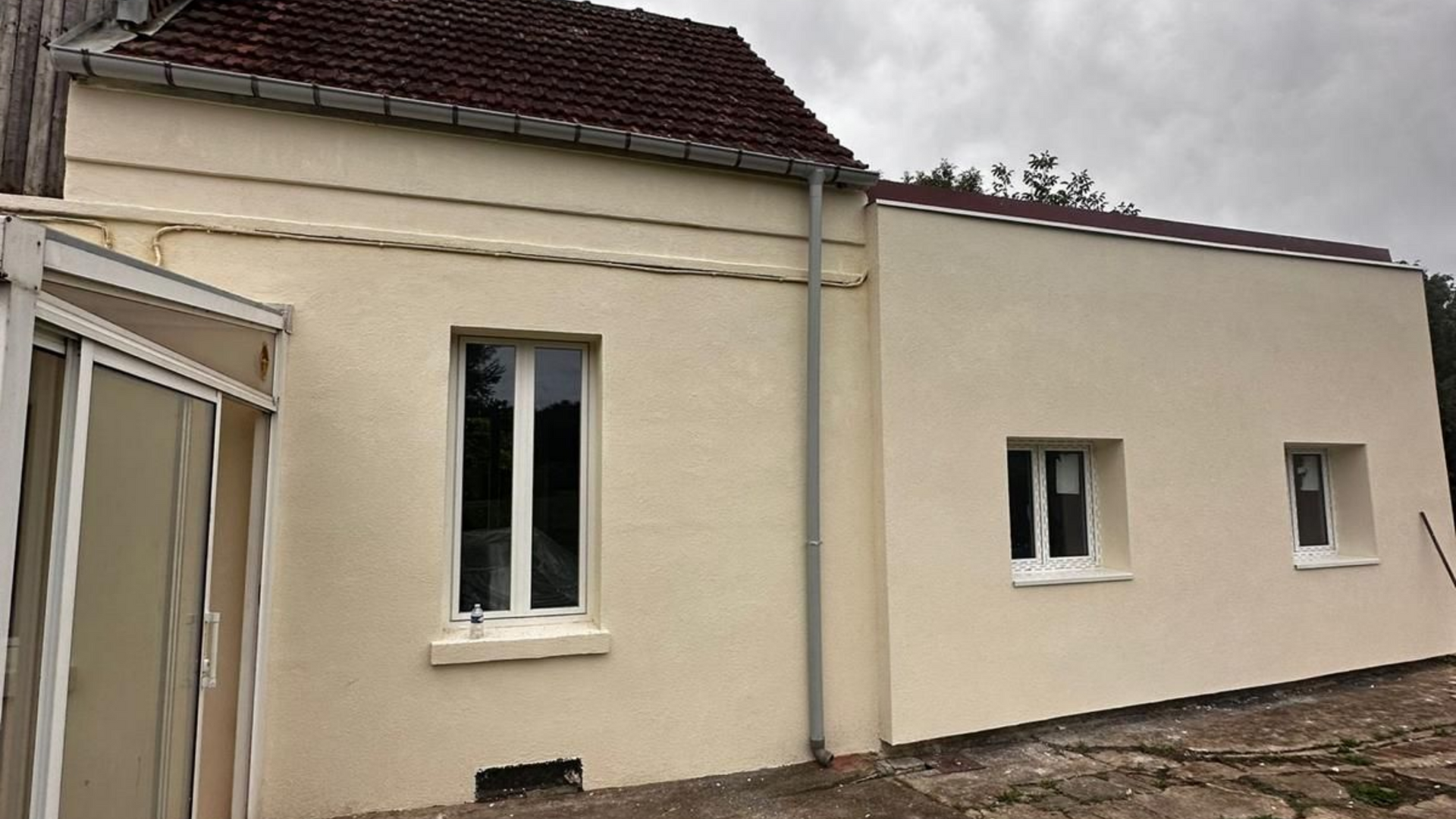 Extérieur d'une maison beige avec un toit de tuiles rouges, deux fenêtres.