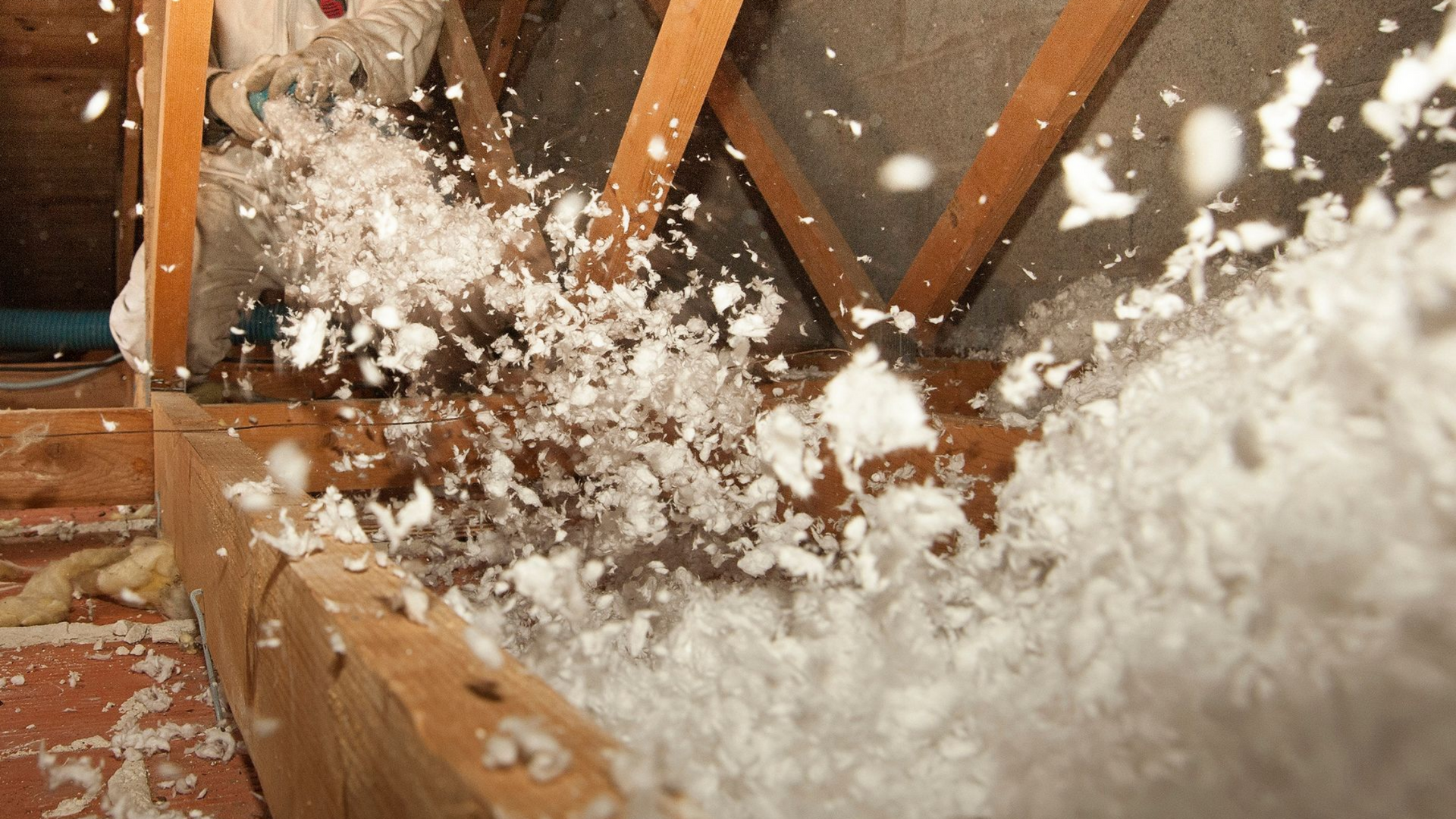 De l'isolant blanc est insufflé dans les combles.