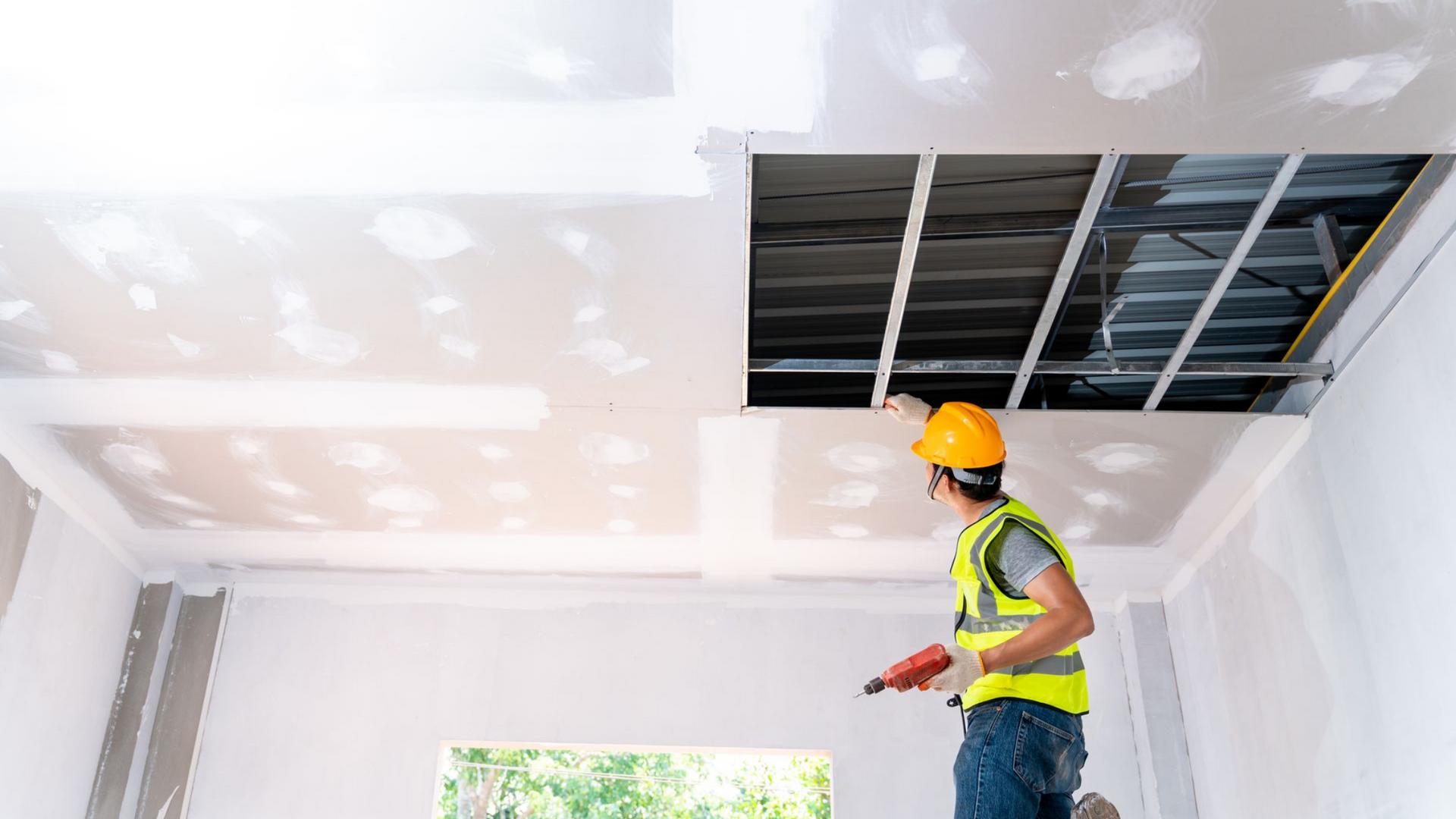 Un ouvrier du bâtiment installe des plaques de plâtre au plafond.