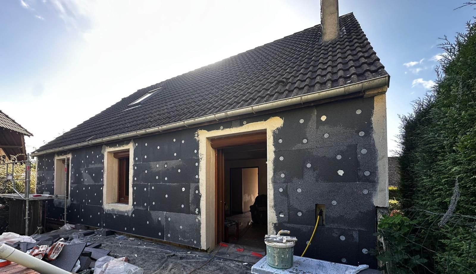Extérieur d'une maison en rénovation, avec des panneaux d'isolation appliqués sur les murs.