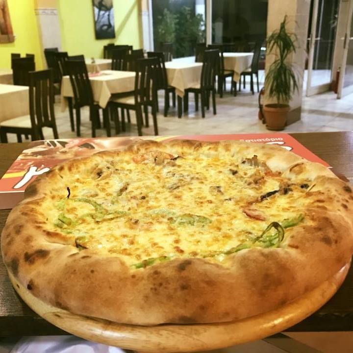 Μεγάλη πίτσα με τυρί σε τραπέζι σε ένα χαλαρό εστιατόριο με καρέκλες και φυτά στο φόντο