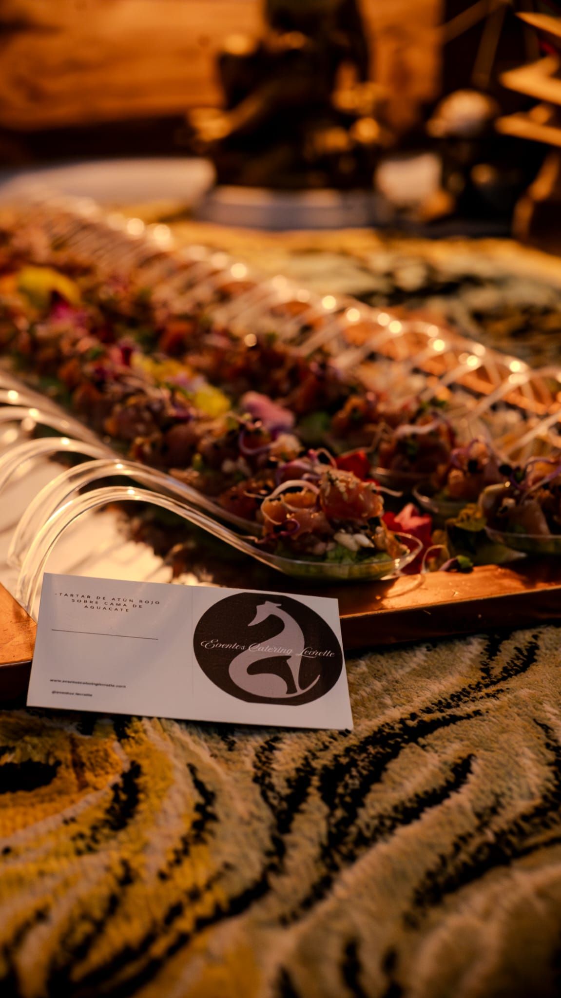 Una bandeja larga de comida con aderezos y un logotipo con una serpiente estilizada, reposa sobre una superficie estampada.