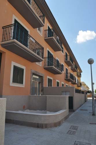 Edificio de apartamentos naranja con balcones a lo largo de una acera tranquila bajo un cielo azul.