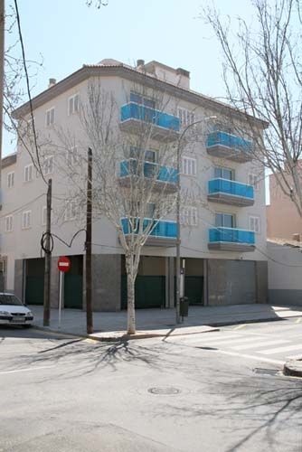 Edificio de apartamentos en esquina con balcones azules en una soleada esquina de la calle.