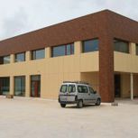 Edificio de ladrillo y color beige con una pequeña furgoneta aparcada delante.