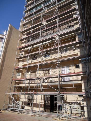 Edificio de apartamentos alto con andamios en la fachada principal bajo un cielo azul despejado.