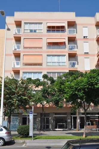 Edificio de apartamentos de cinco pisos color melocotón con balcones y árboles al frente bajo un cielo azul.