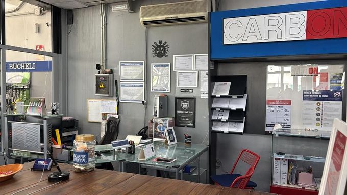 Mostrador de oficina pequeño con mampara de cristal, papeleo, letreros y una ventanilla de atención al público azul