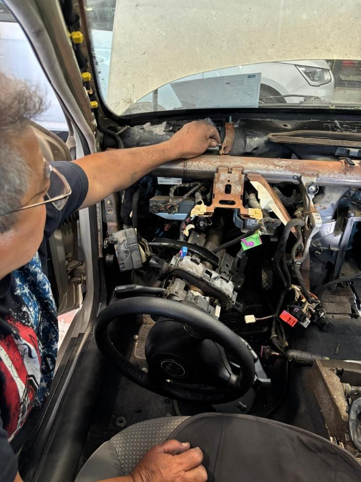 Mecánico metiendo la mano en el salpicadero desmontado de un coche durante una reparación interior.