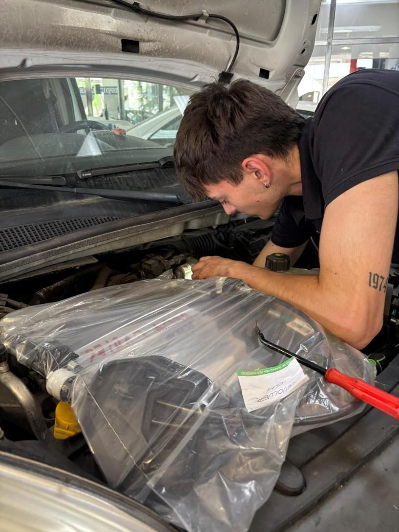 Mecánico inclinado sobre el capó abierto de un coche, trabajando en un motor envuelto en un garaje.