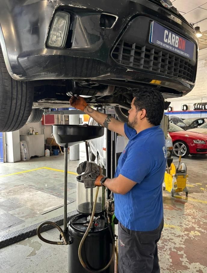 Mecánico con camisa azul inspeccionando un coche en un elevador en un taller mecánico.