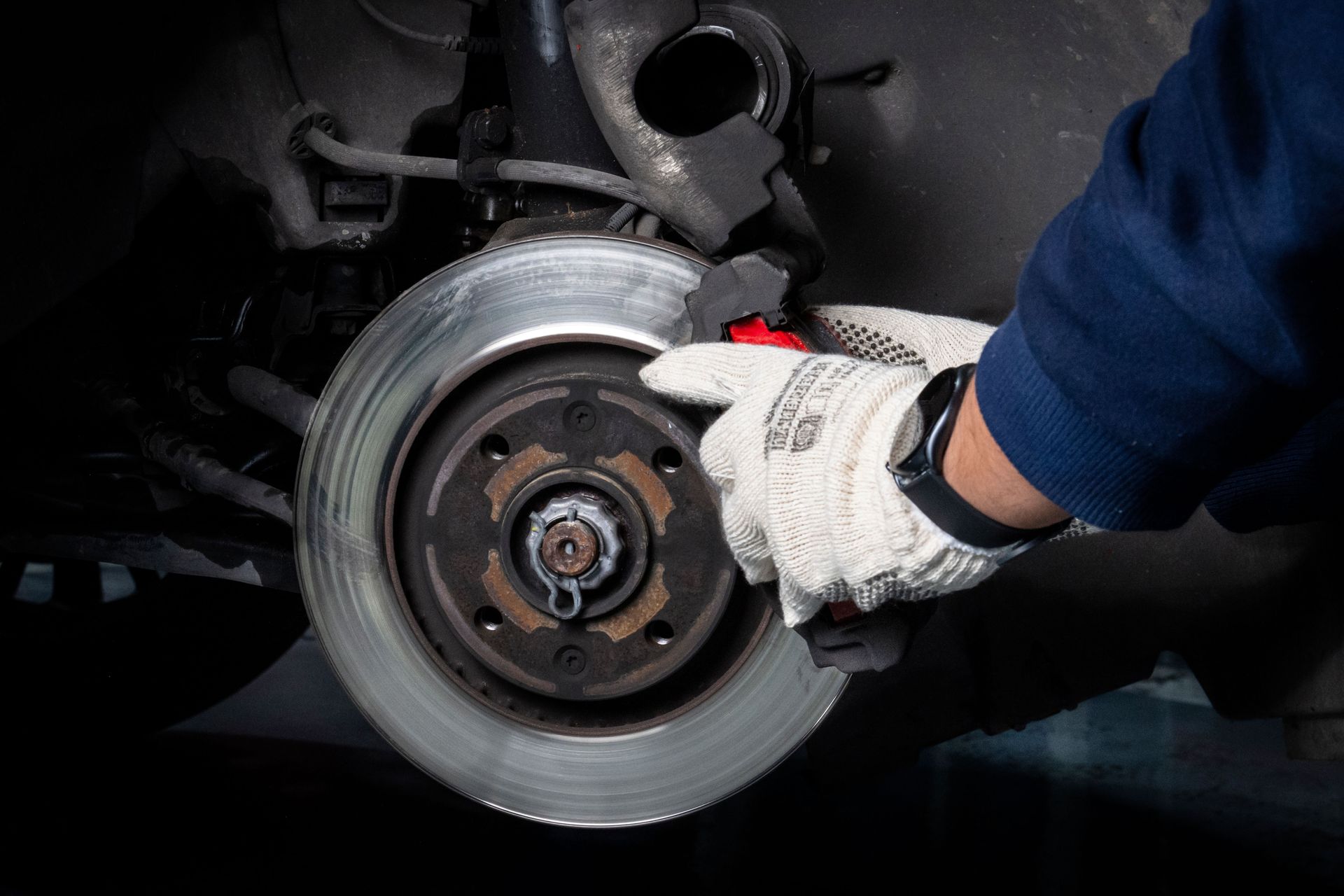 Manos enguantadas de un mecánico inspeccionando un disco de freno y un cubo de rueda de un automóvil.