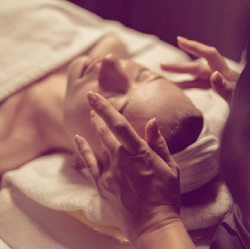 Persona recibiendo un masaje facial con una toalla blanca sobre la cabeza en un entorno de spa.
