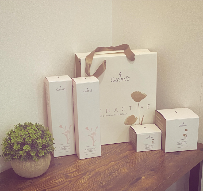 Bolsas y cajas de regalo con productos de spa sobre una mesa de madera junto a una pequeña planta en maceta.