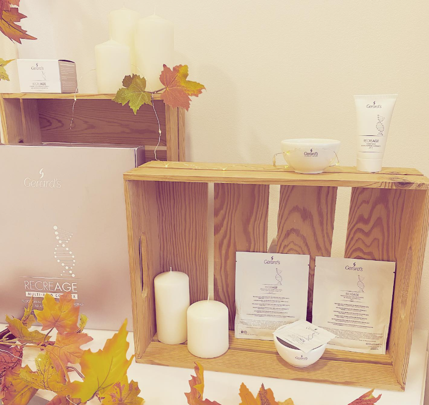 Estanterías de madera con hojas de otoño, velas y productos para el cuidado de la piel sobre un fondo beige cálido.