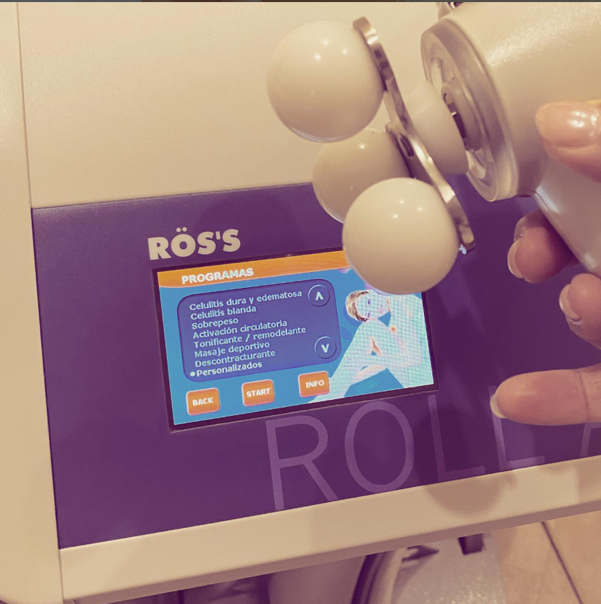 Una mano sostiene un dispositivo de masaje blanco sobre una pantalla morada de ROS'S con detalles del producto.