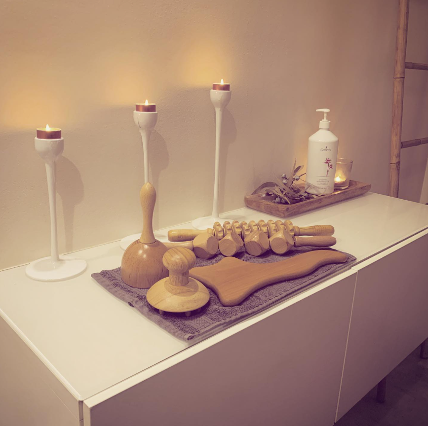 Mesa de spa con velas, herramientas de masaje y una botella de loción blanca sobre una superficie ordenada.