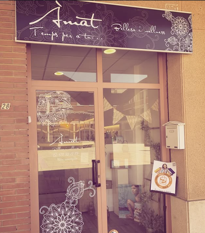 Fachada de tienda con puerta de cristal, letrero morado y exterior de ladrillo, decorada con diseños florales blancos.