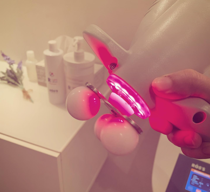 Una mano sostiene un juguete rosa brillante con forma de flor y bombillas redondas blancas en una habitación