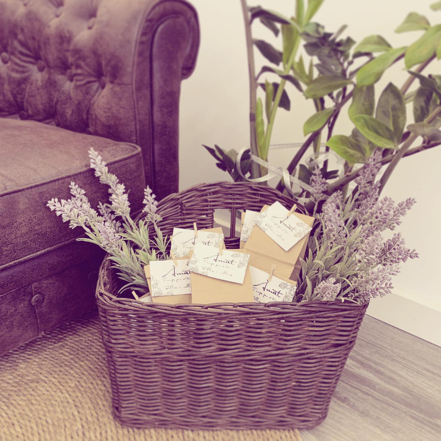 Cesta de mimbre con lavanda y bolsas de regalo junto a un sofá de terciopelo morado en el interior.