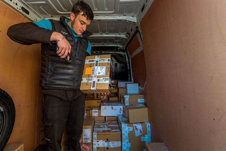 Une personne charge des cartons empilés à l'intérieur d'une camionnette
