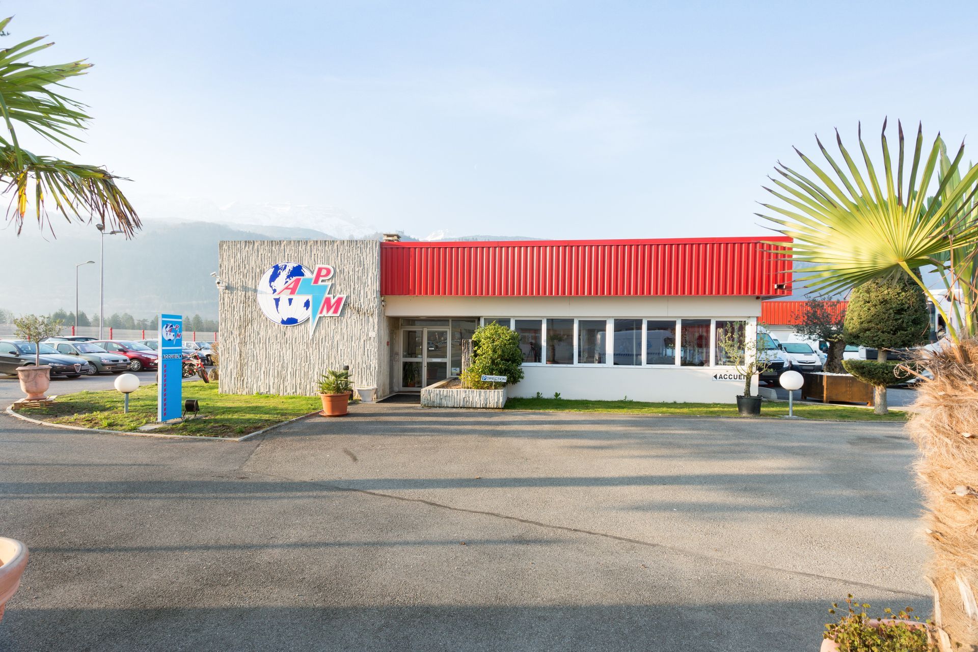 Petit bâtiment en bord de route avec un auvent rouge, une façade en pierre et des palmiers, près d'une route au bord de l'eau.