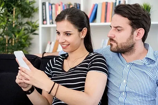 Un hombre y una mujer están sentados en un sofá mirando un teléfono celular.