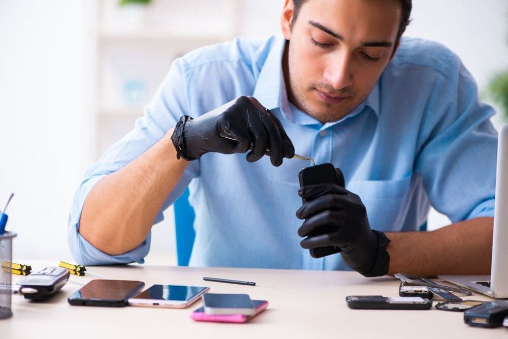 Un hombre que lleva guantes negros está reparando un teléfono celular.