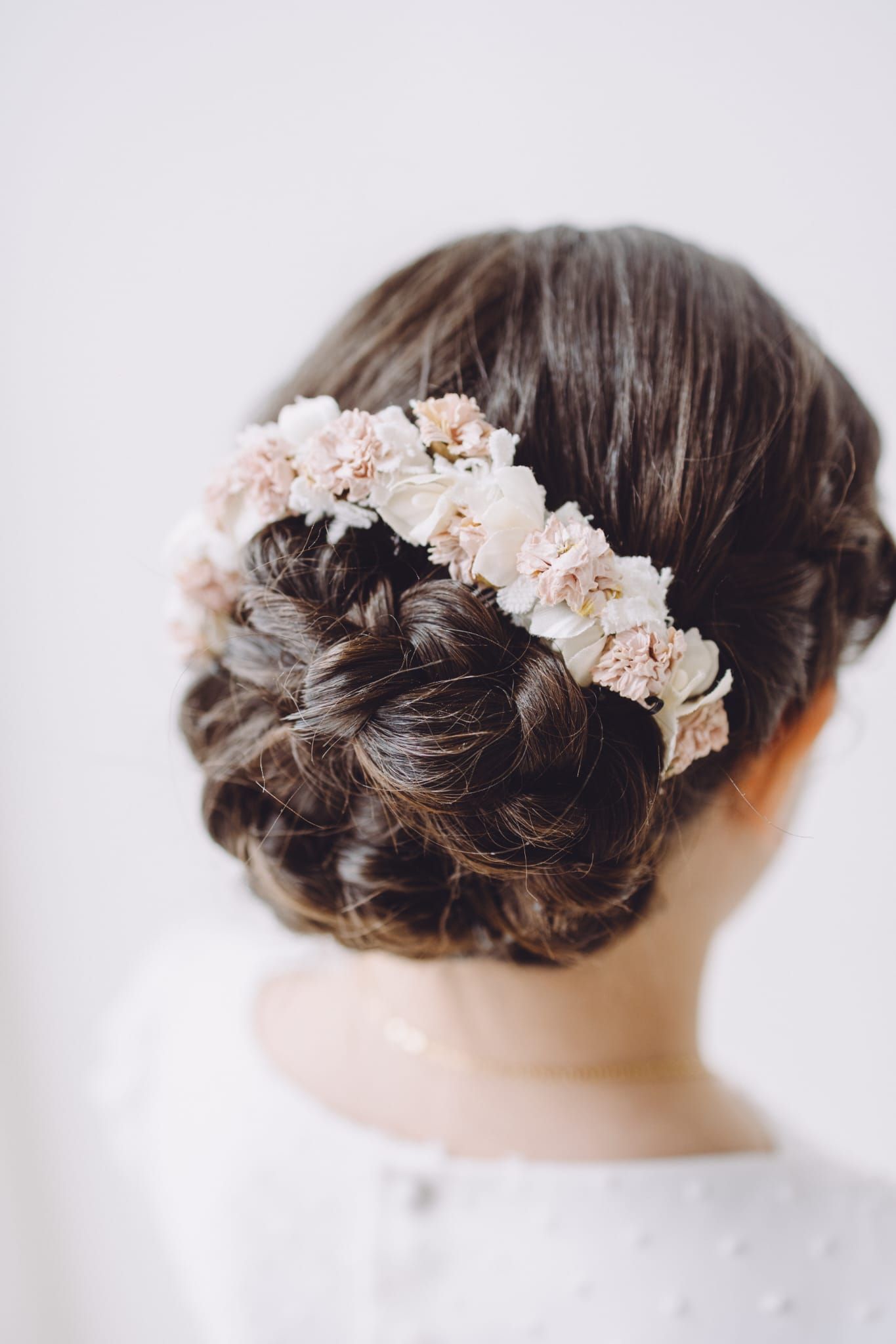 Mujer con cabello oscuro recogido, adornado con una corona de flores, sobre un fondo blanco.