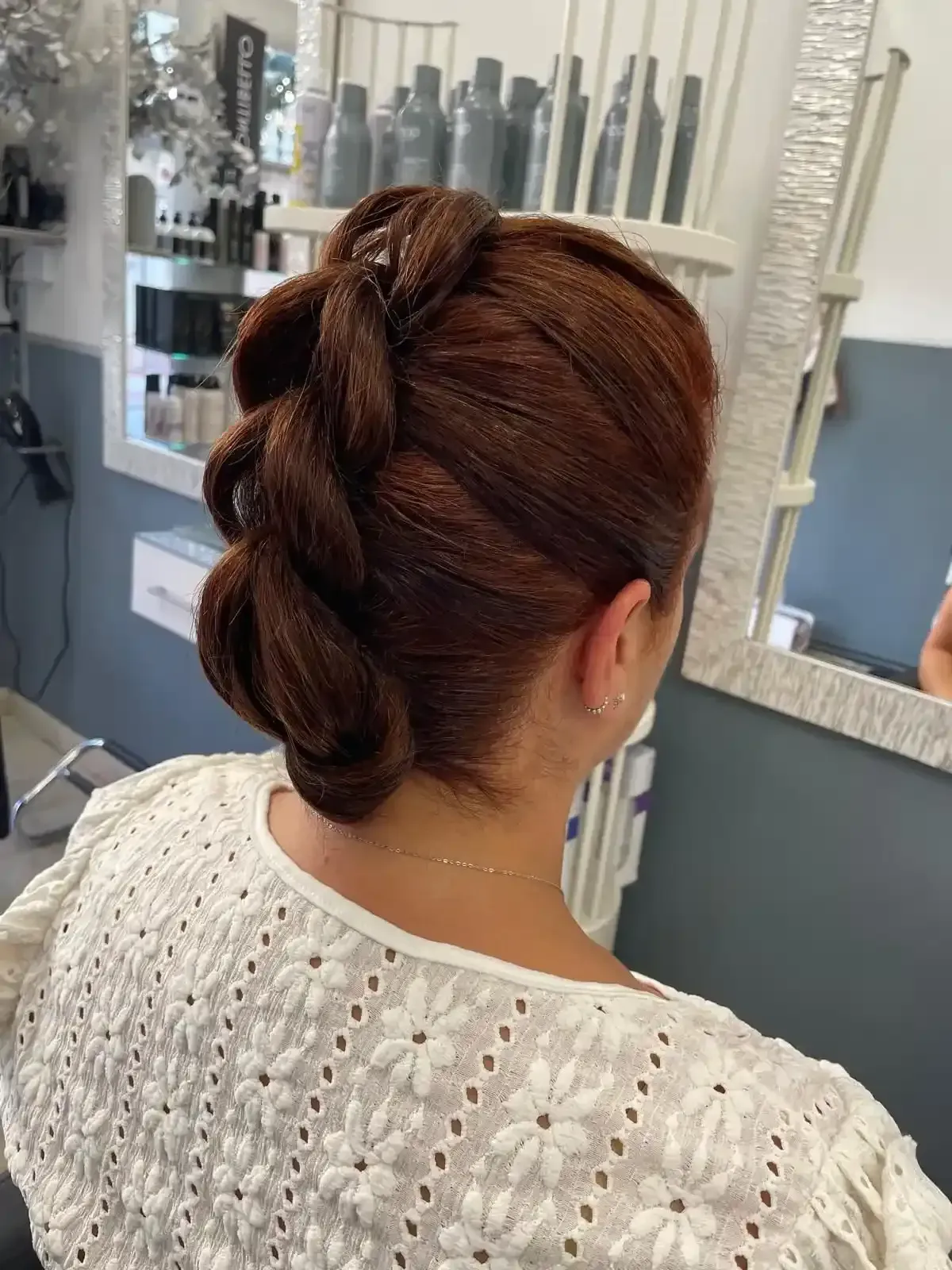 Mujer con cabello castaño rojizo recogido en una trenza y un top blanco con ojales. En un salón de belleza.