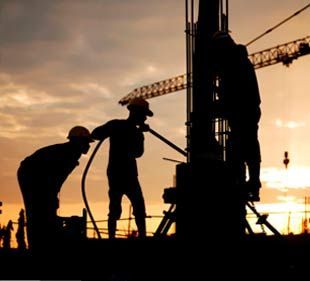 Un grupo de trabajadores de la construcción está trabajando en un sitio de construcción al atardecer.