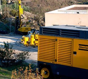 Un compresor de aire Atlas Copco amarillo está estacionado frente a un edificio.