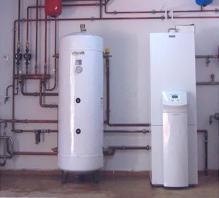 Dos calderas blancas están ubicadas una al lado de la otra en una habitación con tuberías.