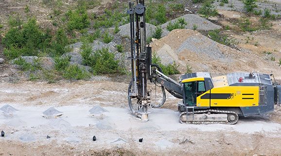 Un taladro amarillo y gris está sentado sobre un campo de tierra.
