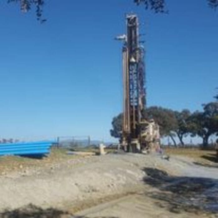 Un gran taladro se encuentra en la cima de una colina de tierra al lado de un río.