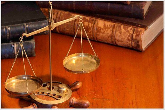 Una balanza de la justicia reposa sobre una mesa de madera junto a una pila de libros.