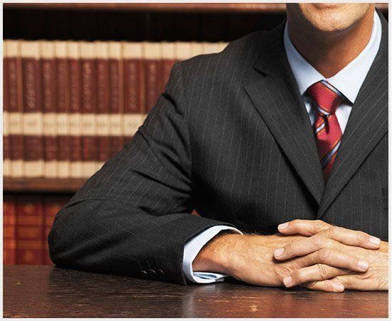 Un hombre con traje y corbata está sentado en un escritorio con las manos cruzadas.