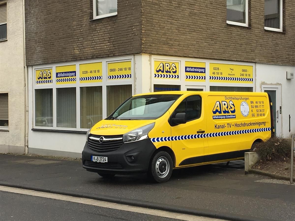 Ein gelber Lieferwagen mit der Aufschrift „APS“ steht vor einem Gebäude