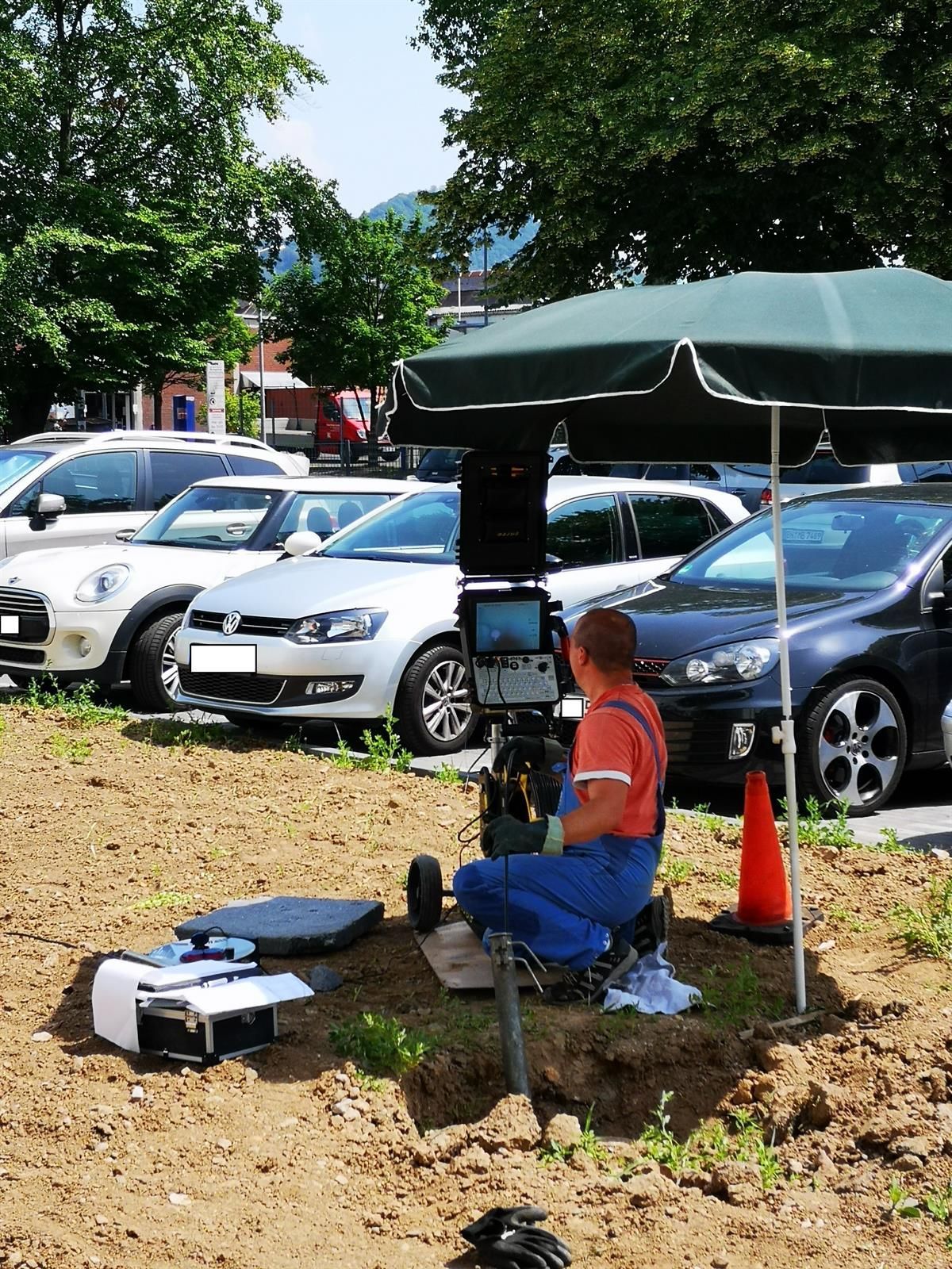 Ein Mann sitzt im Dreck unter einem Regenschirm auf einem Parkplatz