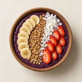 Smoothie bowl morado cubierto con plátano, fresas, virutas de coco y granola.