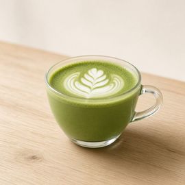 Latte de matcha verde con arte latte en una taza de vidrio transparente sobre una mesa de madera.