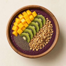 Smoothie bowl morado con mango, kiwi, granola y semillas de chía en un tazón de madera.