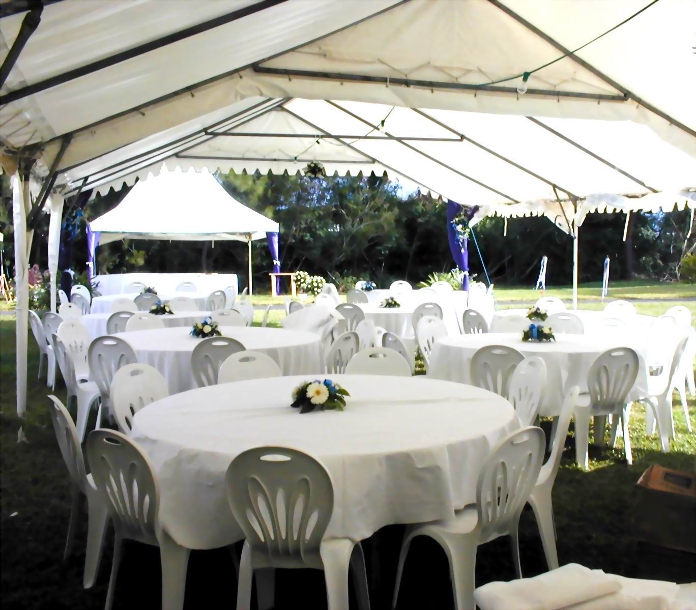 Des tables pour un évènement avec nappe blanche et couverts sous un chapiteau.