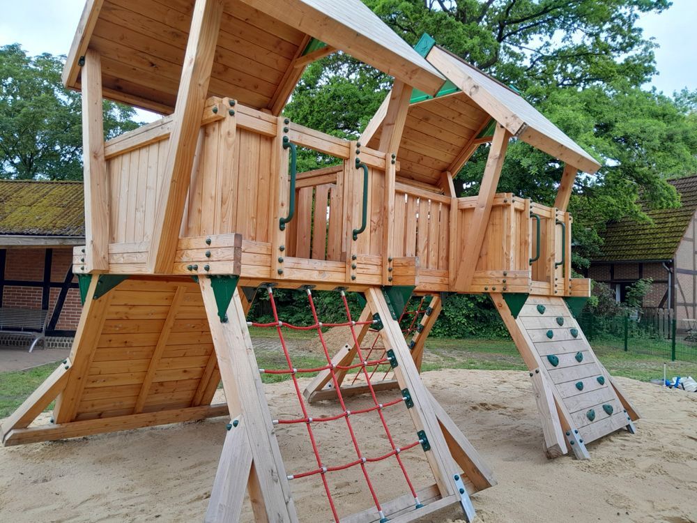 ein Holzgebäude mit einem Zaun davor und einem Traktor dahinter - Spielplatzprüfung Franziska Müller aus Lüchow im Wendland