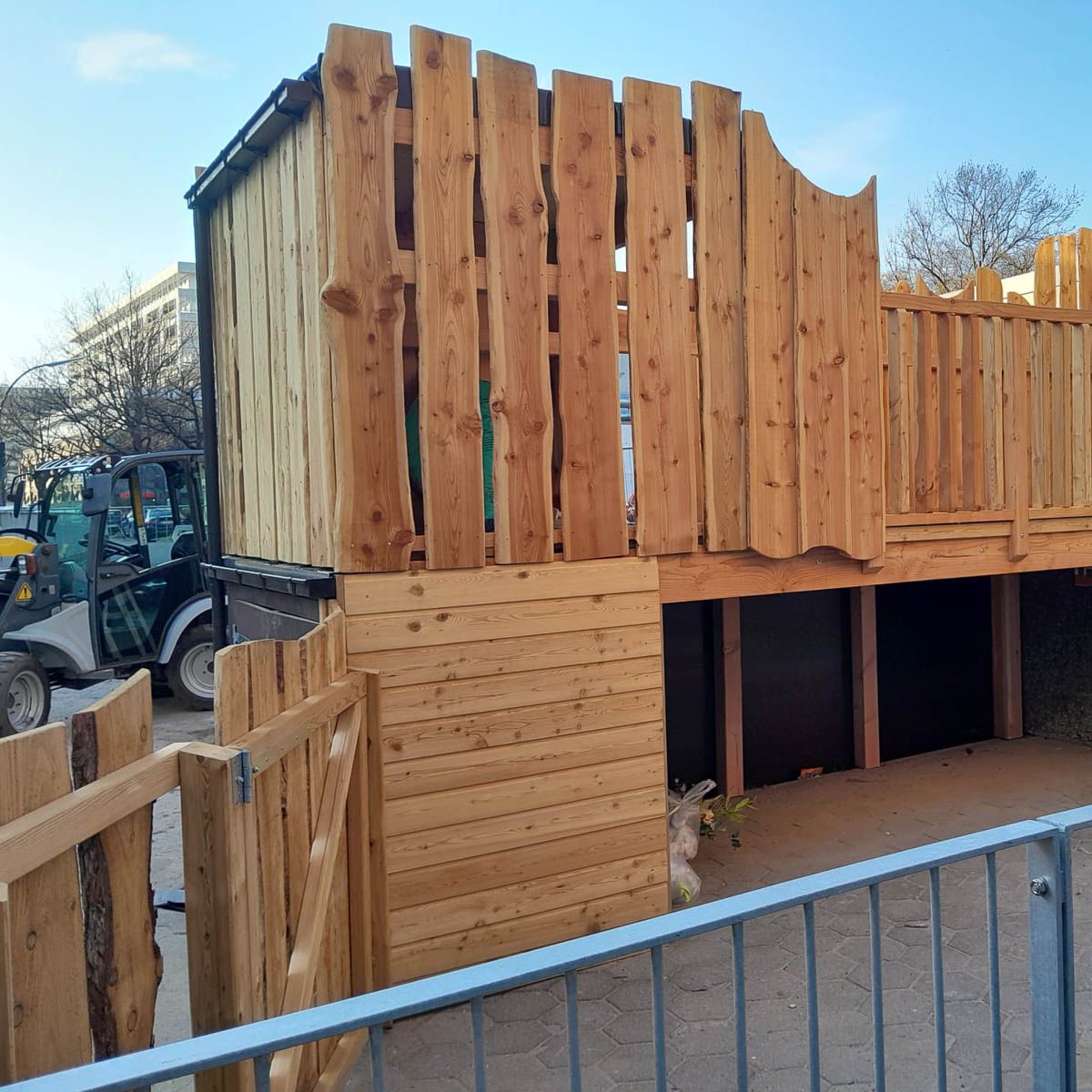 ein Holzgebäude mit einem Zaun davor und einem Traktor dahinter - Spielplatzprüfung Franziska Müller aus Lüchow im Wendland