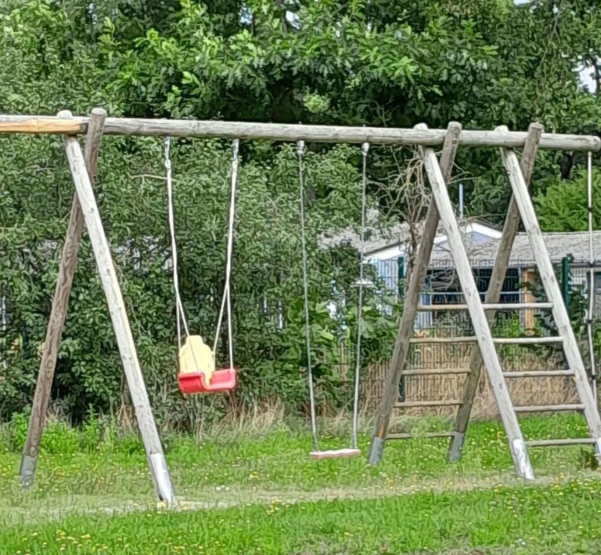 ein Holzspielplatz mit Schaukeln im Gras - Spielplatzprüfung Franziska Müller aus Lüchow im Wendland