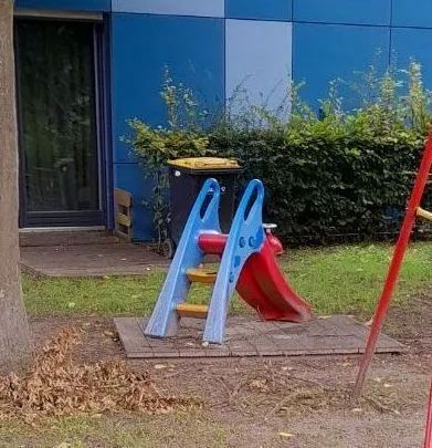ein Spielplatz mit einer Rutsche und Schaukel vor einem Gebäude -Spielplatzprüfung Franziska Müller aus Lüchow im Wendland