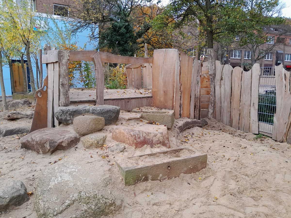 ein Holzzaun umgibt einen Sandplatz mit Steinen und Bäumen - Spielplatzprüfung Franziska Müller aus Lüchow im Wendland