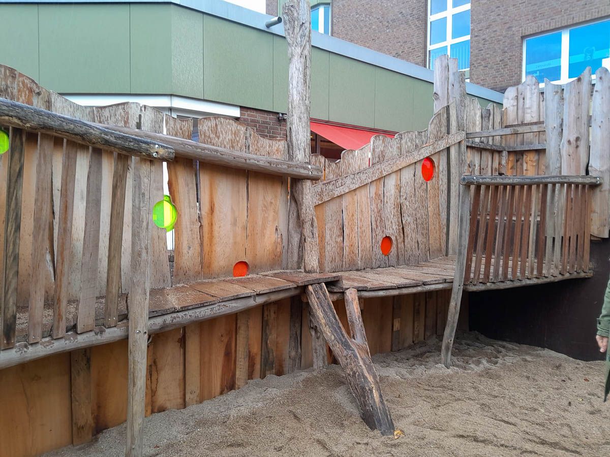 ein Holzspielplatz mit einem Gebäude im Hintergrund - Spielplatzprüfung Franziska Müller aus Lüchow im Wendland